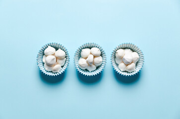 White mini meringue cookies in blue paper cup on blue background.