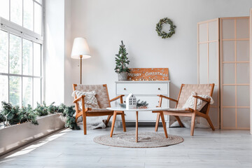 Interior of light living room with armchairs, table and Christmas decorations