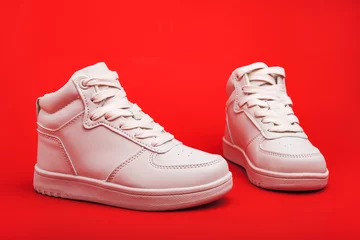  pair of white youth sneakers on red background close-up. © kosoff