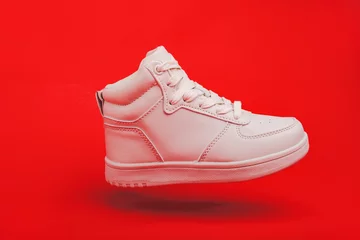 Foto op Canvas Sports youth shoes on red background close-up. white leather lace-up sneakers. © kosoff