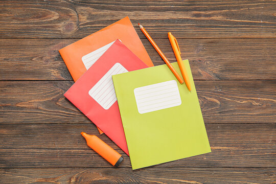 Different colorful notebooks with stationery on brown wooden background
