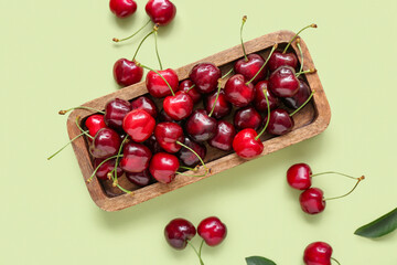 Board with sweet cherries on green background