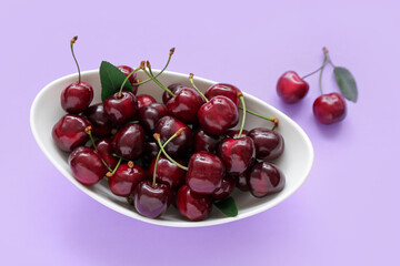 Bowl with sweet cherries on lilac background
