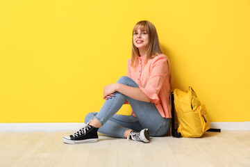 Female student with backpack sitting near yellow wall