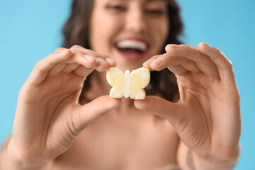 Young woman with marshmallow in shape of butterfly on blue background, closeup