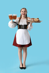 Beautiful Octoberfest waitress with beer and snacks on blue background