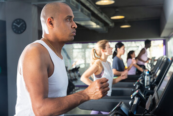 Fototapeta na wymiar Portrait of sporty young adult man running on treadmill in gym