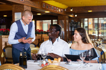 Elegant man waiter receiving order from guests in fashionable restaurant
