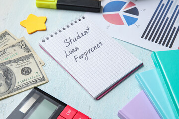 Notepad with text STUDENT LOAN FORGIVENESS, calculator, dollar banknotes and chart on green table