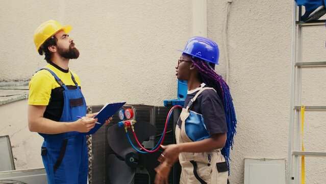 Precise servicemen working with pressure indicators to check condenser refrigerant levels, writing result on clipboard. Proficient experts using barometer benchmarking air conditioner tool