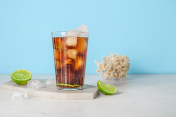 Board with glass of cold Cuba Libre cocktail and coral on white table