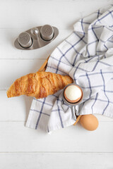 Holder with boiled chicken egg and croissant on white wooden background