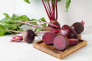 Wooden board of fresh beets with green leaves on light background