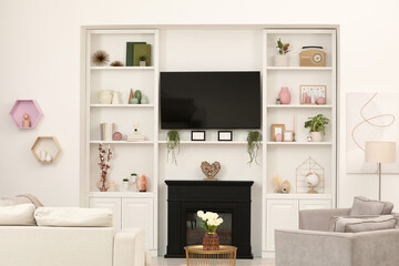 Stylish room interior with beautiful fireplace, TV set, sofa, armchairs and shelves with decor