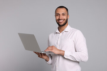 Smiling young man with laptop on grey background