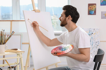 Man painting in studio. Using easel to hold canvas