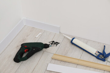 Plinths, caulking gun, screwdriver and screws on laminated floor in room
