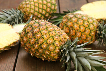 Whole and cut ripe pineapples on wooden table, closeup