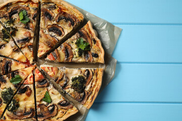 Delicious quiche with mushrooms and parsley on light blue wooden table, top view. Space for text