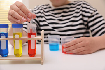 Girl mixing colorful liquids at white table indoors, selective focus. Kids chemical experiment set
