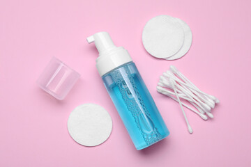 Bottle of face cleansing product, cotton buds and pads on pink background, flat lay. Space for text