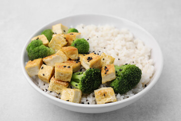 Bowl of rice with fried tofu and broccoli on white table, closeup
