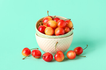 Bowl with sweet yellow cherries on turquoise background
