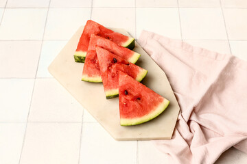 Board with pieces of fresh watermelon on white tile background