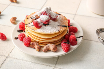 Plate of tasty pancakes with raspberries and nuts on white tile background