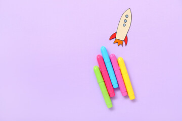 Markers with paper rocket on purple background