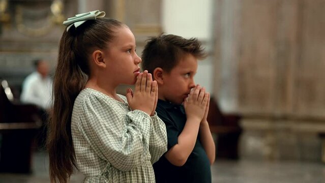Dos Niños hermanos amigos católicos cristianos rezando meditando orando  en familia con sus manos juntas hincados de rodillas pidiendo a Dios en basilica templo iglesia santuario