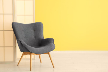 Stylish black armchair and folding screen near yellow wall