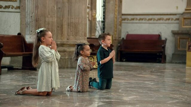 Ni&ntilde;os hermanos amigos cat&oacute;licos cristianos rezando meditando orando  en familia con sus manos juntas hincados de rodillas pidiendo a Dios en basilica templo iglesia santuario