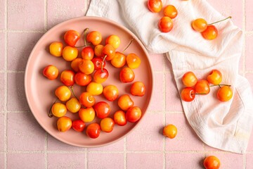 Plate with sweet yellow cherries on pink tile background