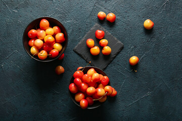 Fototapeta na wymiar Bowls with sweet yellow cherries on dark background