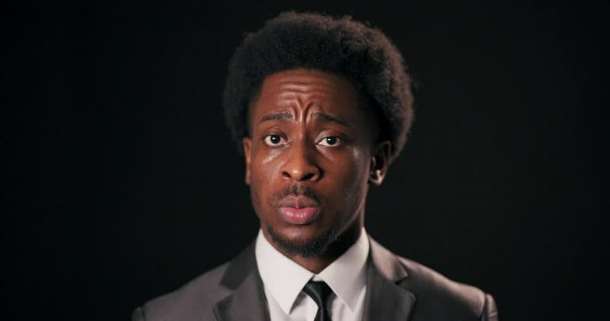 African man in smart suit stands over black background in studio looking directly at camera with fearful expression diplomat entrepreneur feeling anxious about high stakes involved in his work.