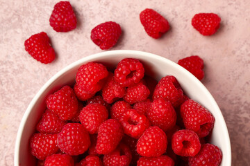 Bowl with fresh raspberries on pink background