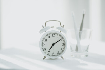 The toothbrushes in a glass and alarm clock  with copy space in bathroom