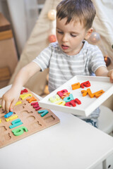 Male kid playing with wooden eco friendly alphabet letters board on table top view intellectual game