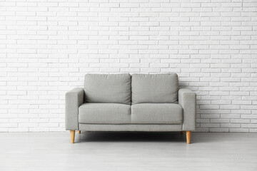 Cozy grey sofa near white brick wall
