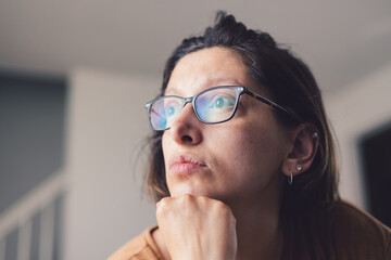 Young millennial mother at home wearing prescription glasses looking of into distance sad and...