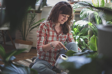 A young woman enjoys caring for flowers. Watering indoor plants and admiring them.
