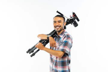 a cameraman in plaid shirt carrying one set of camera on his shoulder and smiling