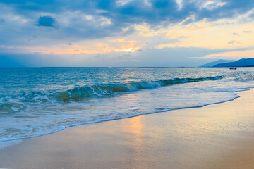 Sunset on the Sanya beach, the sun shines through the clouds on the golden sea and beach
