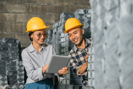 Asian women and men company employees wearing safety helmets use together a digital tablet in a storage warehouse