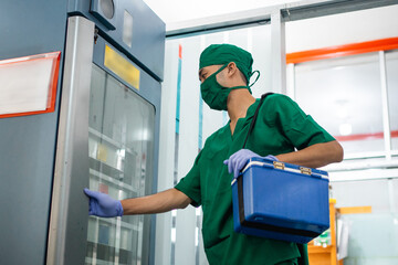 man in sterile clothes and mask carrying a blood bag box opens the blood quarantine cabinet in the laboratory room