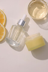Glass dropper bottle displayed with a yellow jar and a bowl of essential oil extracted from Lemon (Citrus limon). Mockup of serum skin care cosmetic of beauty facial