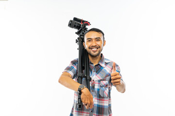 a smiling cameraman in plaid shirt standing with thumb up and carrying one set of camera on his...