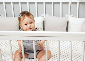 Happy little girl in gray bodysuit sitting in her crib. Baby in a crib. High quality photo