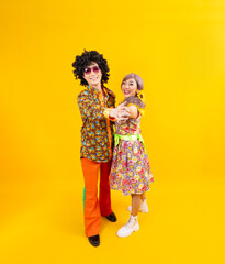 Asian hippie couple dress in 80s vintage fashion with colorful retro clothing while dancing together isolated on yellow background for fancy outfit party and pop culture